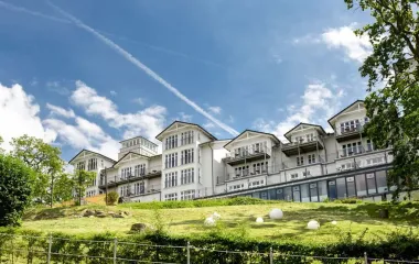 Exterior view of the Vju Hotel with classic architecture, large windows and balconies, situated on a green hill with a well-tended landscape.