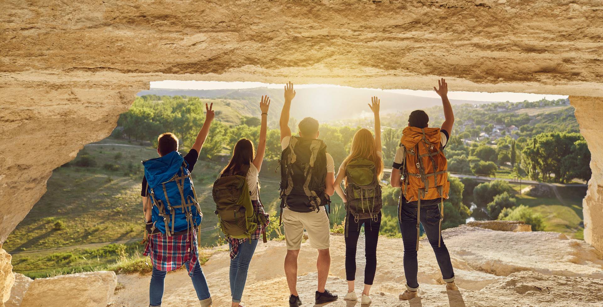 Gruppe von Wanderern hebt die Hände im Sonnenuntergang mit Rucksäcken auf einem Felsvorsprung mit Aussicht.
