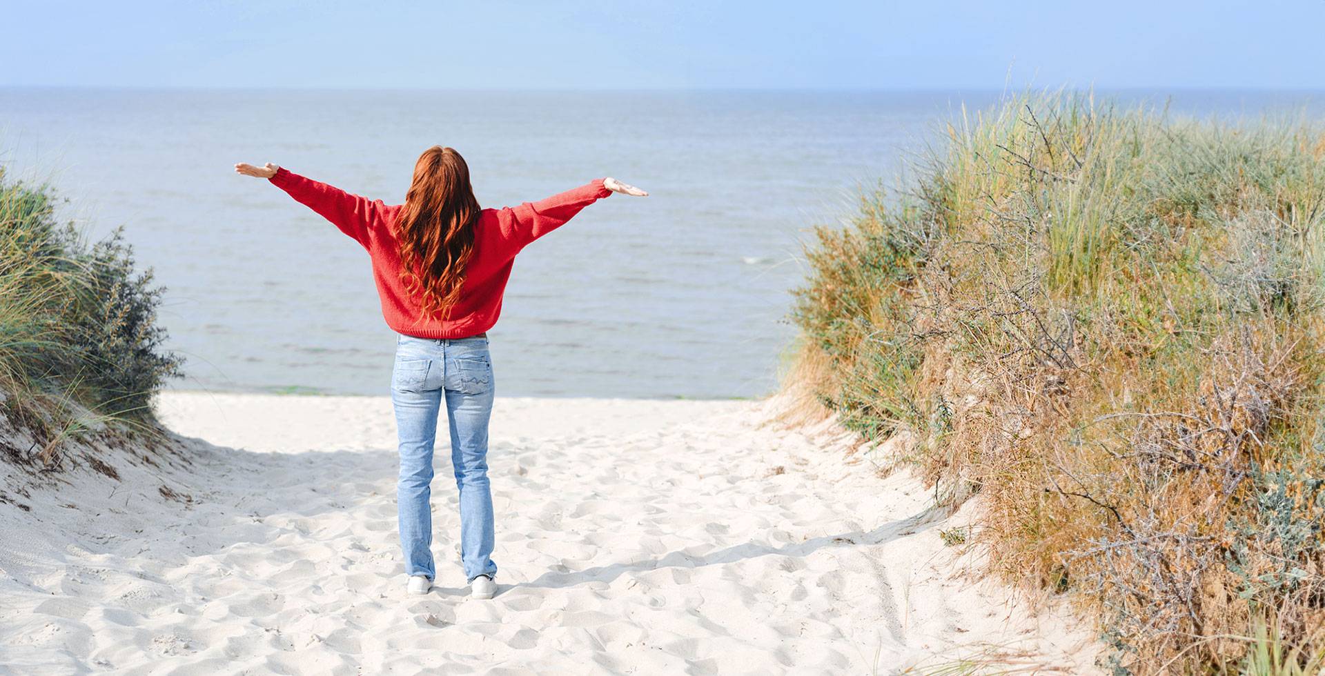 Frau steht am Strand mit ausgestreckten Armen, Blick aufs Meer, symbolisiert Freiheit und neue Möglichkeiten.