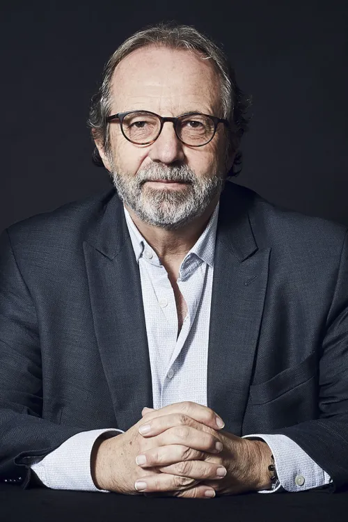 Stephan Gerhard with glasses and a suit sits with his hands folded, a serious facial expression.