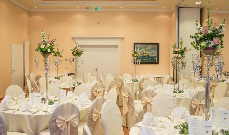 Festlich dekorierter Hochzeitssaal im Vju Hotel auf Rügen, mit runden Tischen, Kerzenständern und Blumengestecken.