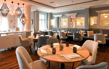 View of the maritime restaurant Küstensilber with light-colored chairs and benches, wooden decor and set tables in the Vju Hotel on Rügen.
