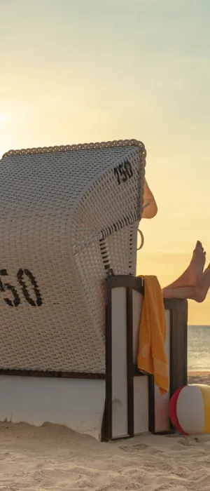 Person relaxing in a beach chair on the Baltic Sea beach at sunset during a summer vacation at the Vju Hotel on Rügen.