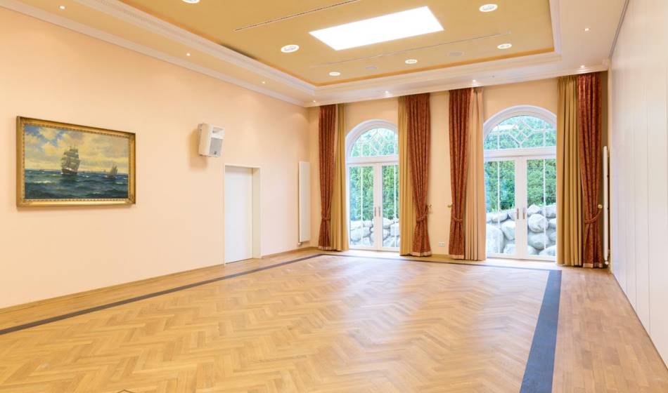 Großer, heller Veranstaltungsraum im Vju Hotel auf Rügen mit Holzboden, großen Fenstern und dezenter Wanddekoration, ideal für Events.