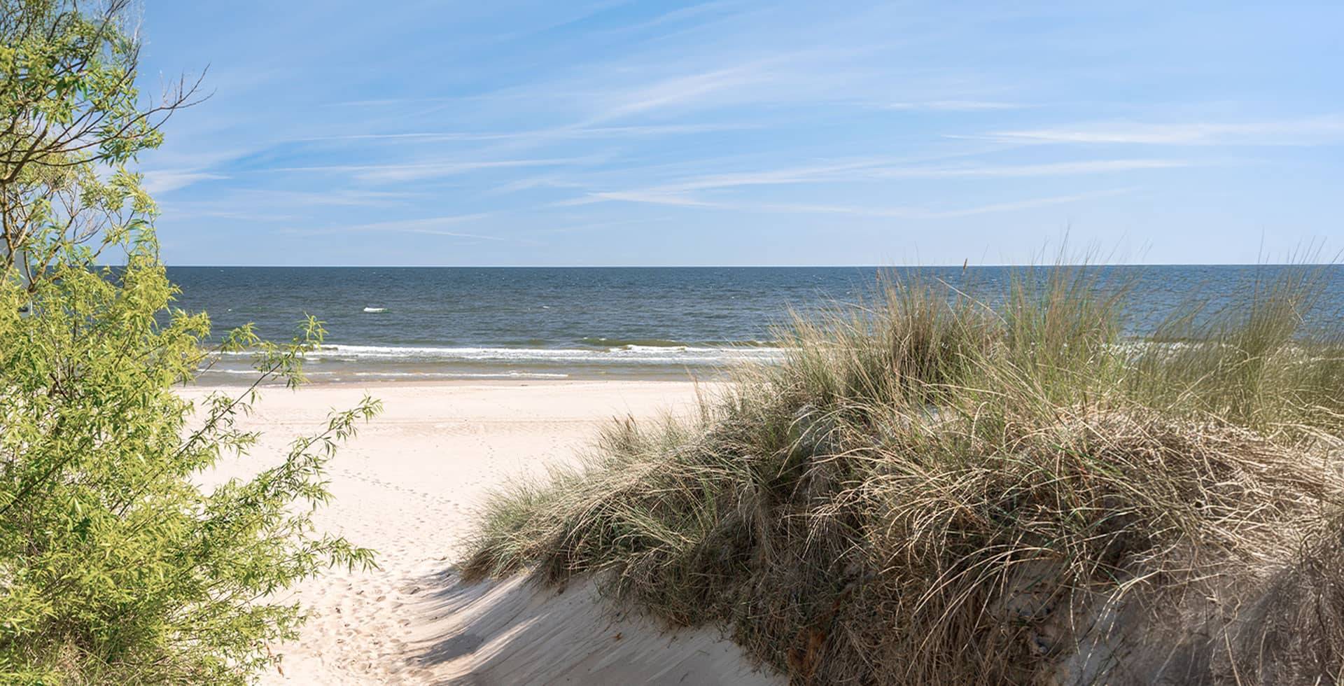 Strandaufgang durch Dünen auf Usedom, ruhiges Meer im Hintergrund.
