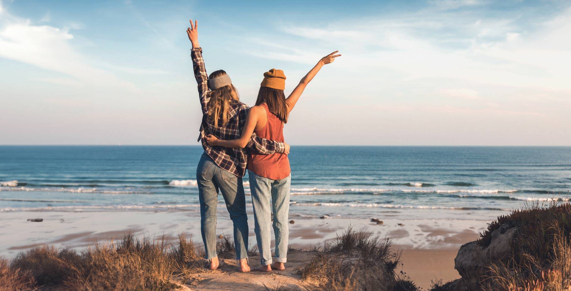 Zwei Personen mit erhobenen Armen blicken von der Ostseeküste aus auf das weite Meer.