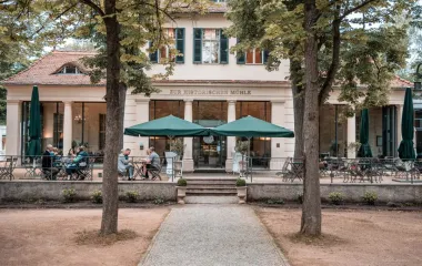 Exterior view of the restaurant Zur historischen Mühle in Potsdam with large terrace, green umbrellas and guests.