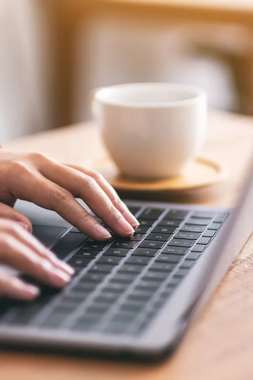Close-up of hands typing on a keyboard with a coffee cup in the background.