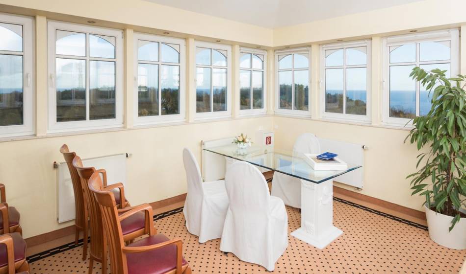 Raum für Trauungen im Vju Hotel auf Rügen, Tisch und Stühle in heller Umgebung, große Fenster mit Ausblick.