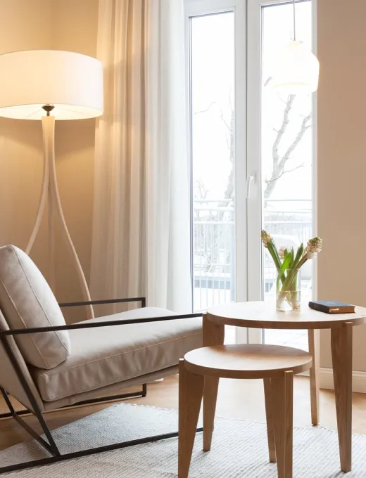 Modern seating area in the Vju Hotel Rügen with a light armchair, wooden side table and large window front.