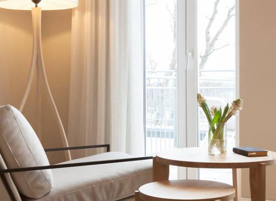 Modern seating area in the Vju Hotel Rügen with a light armchair, wooden side table and large window front.