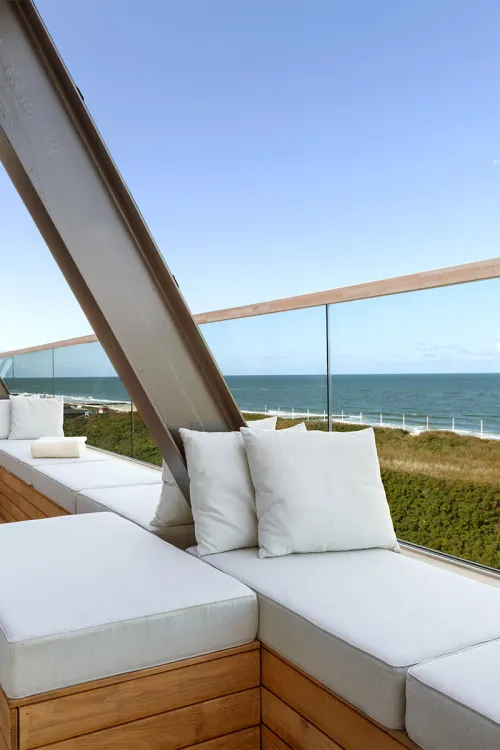 Modern roof terrace with white seating cushions and views of the sea and dunes in the background.