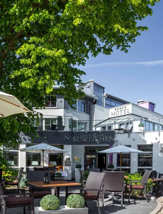 Sunny terrace of the Seezeichen artist quarter in Ahrenshoop with seating and green surroundings.