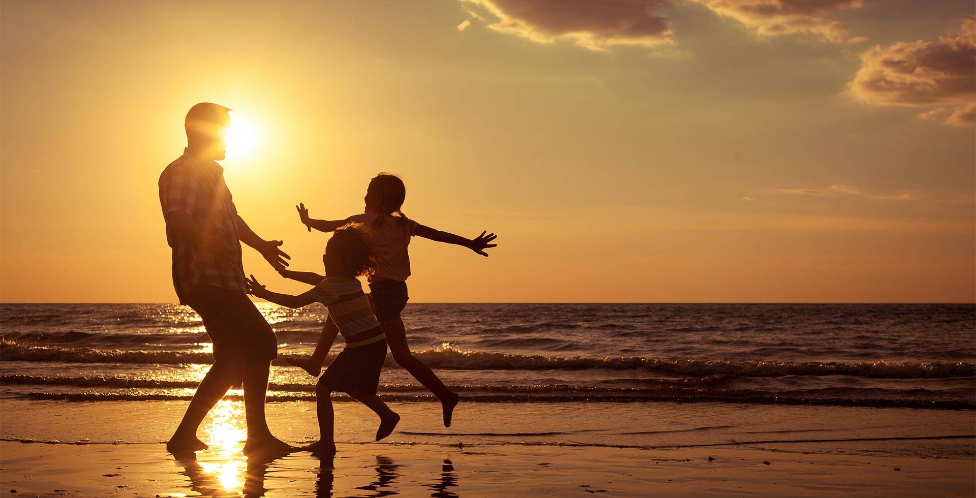 Father plays with his children on the beach at sunset, the silhouettes are visible against the sea.
