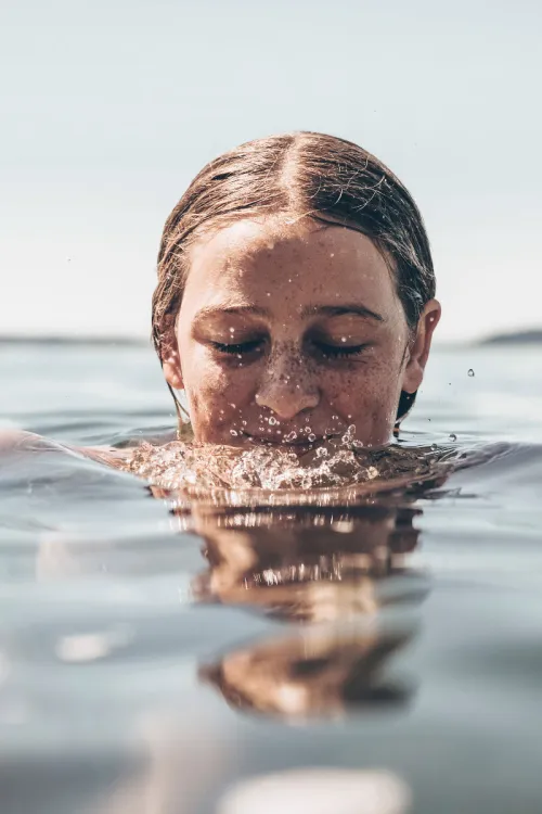 Close-up of a person swimming in water with eyes closed and face slightly submerged.