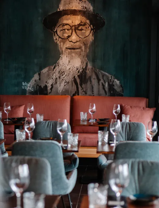 Restaurant with set tables, wine glasses and a large mural of a man in a hat and glasses in the background.