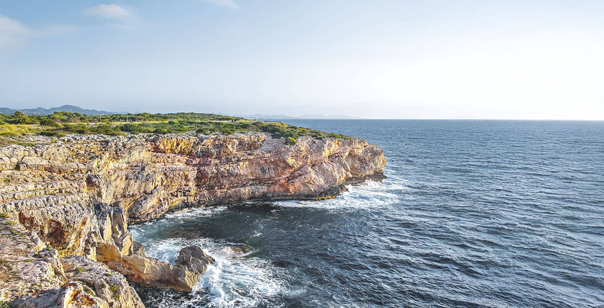 Küstenlandschaft auf Mallorca mit steilen Felsen und ruhigem Meer, umgeben von üppiger Natur.