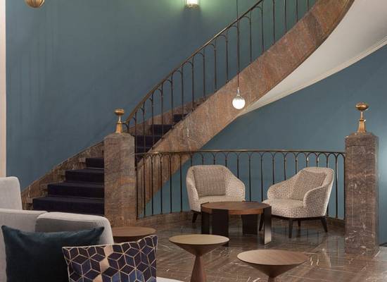 Modern lobby with a curved staircase, stylish armchairs and elegant decor at the Elephant Hotel Weimar.