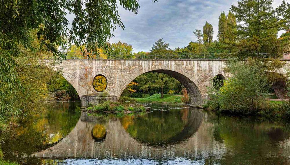 Historische Steinbrücke im Park an der Ilm in Weimar mit Spiegelung im Wasser.