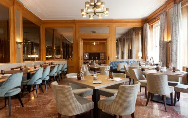 View of the elegant Anna restaurant with light-colored armchairs, wooden decor and laid tables at the Hotel Elephant in Weimar.