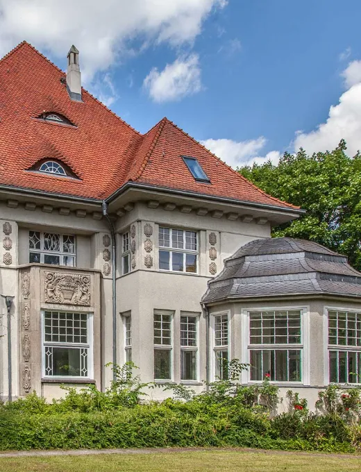 Historic villa with red tiled roof, large windows and decorative facade elements.