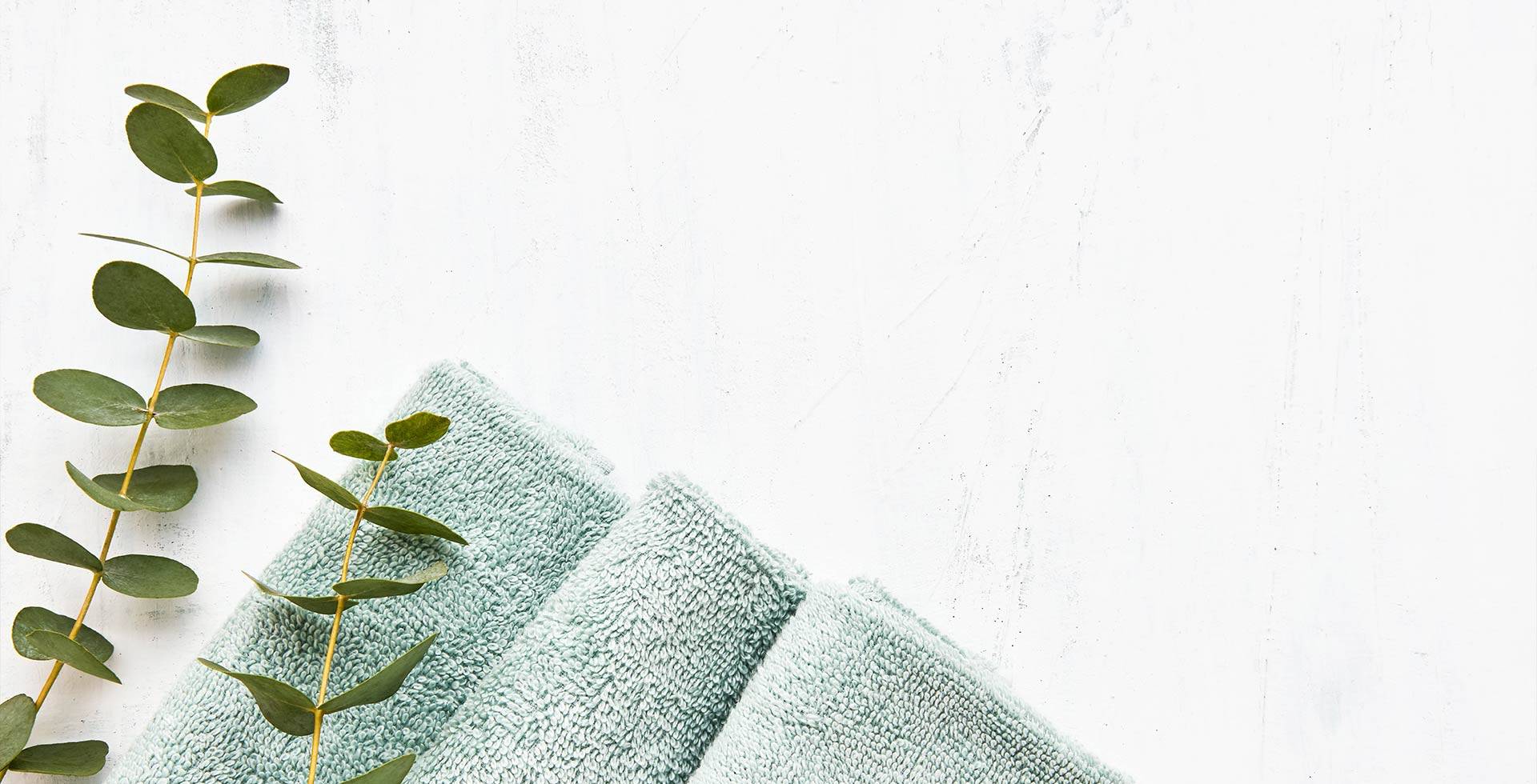 Towels and eucalyptus branch arranged on minimalist light background.
