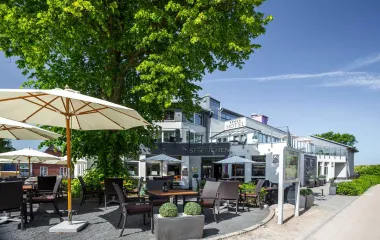 Exterior view of the Seezeichen Hotel in Ahrenshoop with chairs and parasols under a blue sky.
