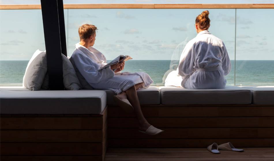 Two people in bathrobes enjoy the sea view on the terrace of the wellness area in the Wyn. on Sylt.