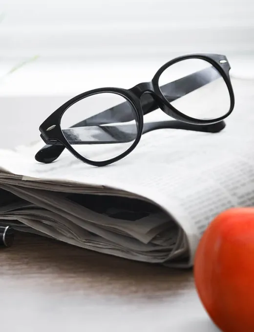 Close-up of glasses lying on a newspaper with an orange detail in the image.