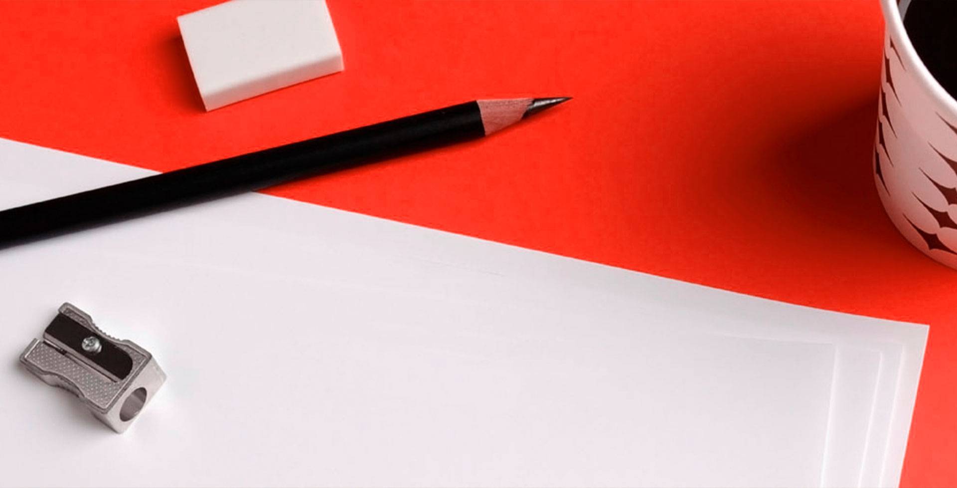 Close-up of a pencil, eraser, sharpener and paper on a desk with a red background.