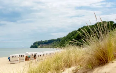 A quiet Baltic Sea beach on Rügen with beach chairs, surrounded by dunes and a green coastal landscape that invites you to relax.