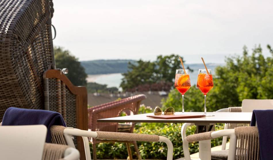 Zwei Aperol-Spritz auf einem Terrassentisch neben einem Strandkorb auf der Seeblick-Terasse im Vju Hotel auf Rügen.