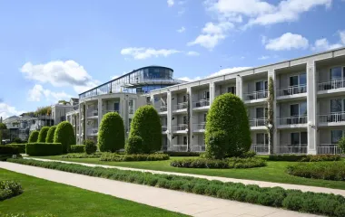 Exterior view of the Hotel Kaiserhof in Heringsdorf with balconies, manicured green spaces and a glass superstructure.