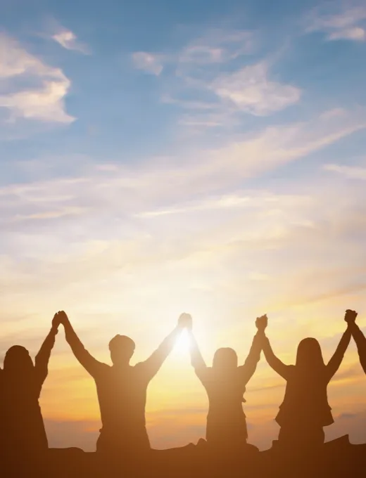 People stand hand in hand and raise their arms in front of a colorful sunset.