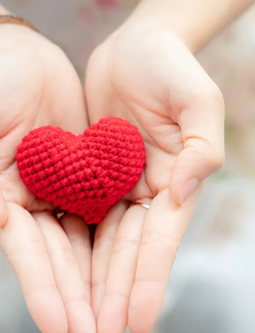 Close-up of hands gently holding a red crocheted heart.