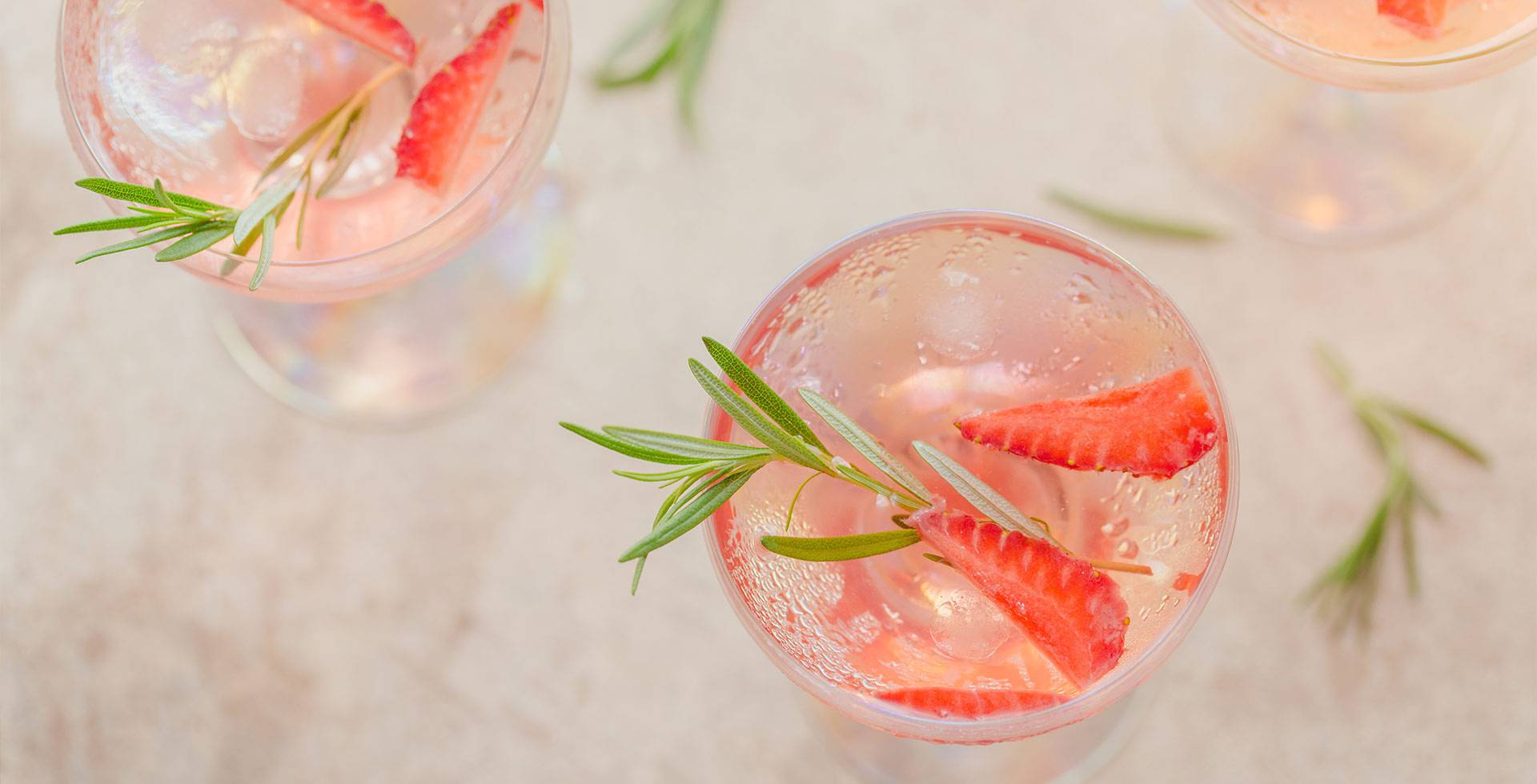 Cocktail with strawberries and rosemary sprig in a glass, photographed from a bird's eye view on a light background.