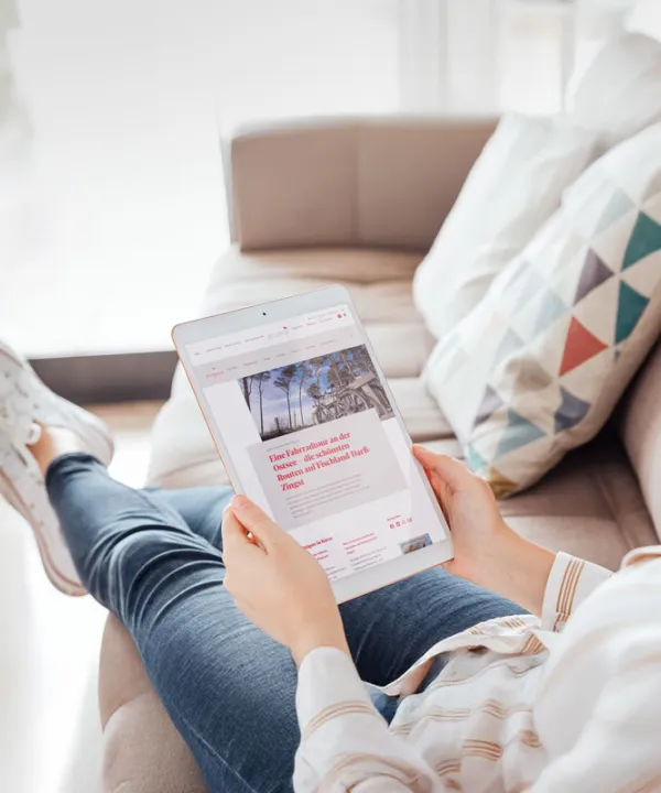 Eine Frau liest, gemütlich auf dem Sofa sitzend, am Tablet im digitalen arcona Magazin.