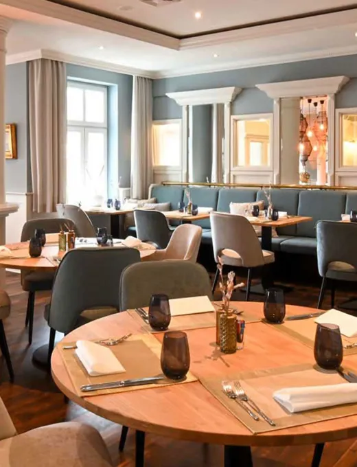 View of the maritime restaurant Küstensilber with light-colored chairs and benches, wooden decor and set tables in the Vju Hotel on Rügen.
