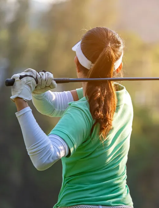 Woman doing a golf swing on a green golf course, concentrated posture and sunny surroundings.
