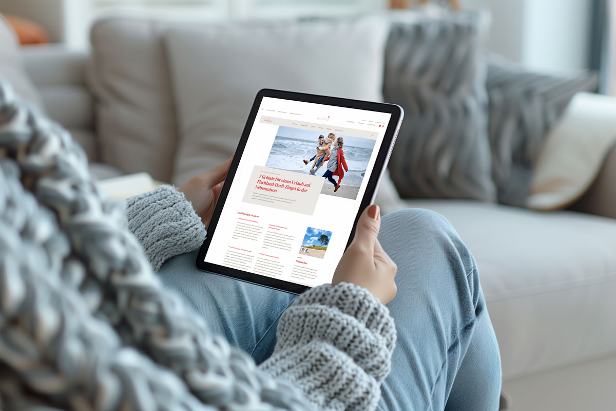 Eine Frau liest, gemütlich auf dem Sofa sitzend, am Tablet im digitalen arcona Magazin.