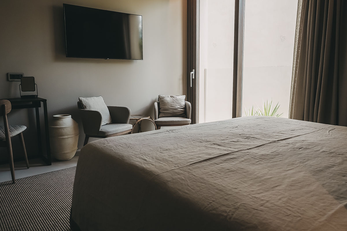 View into the Pequeña Suite of the Barefoot Hotel Mallorca with bed, armchair and balcony, stylish atmosphere for your stay.