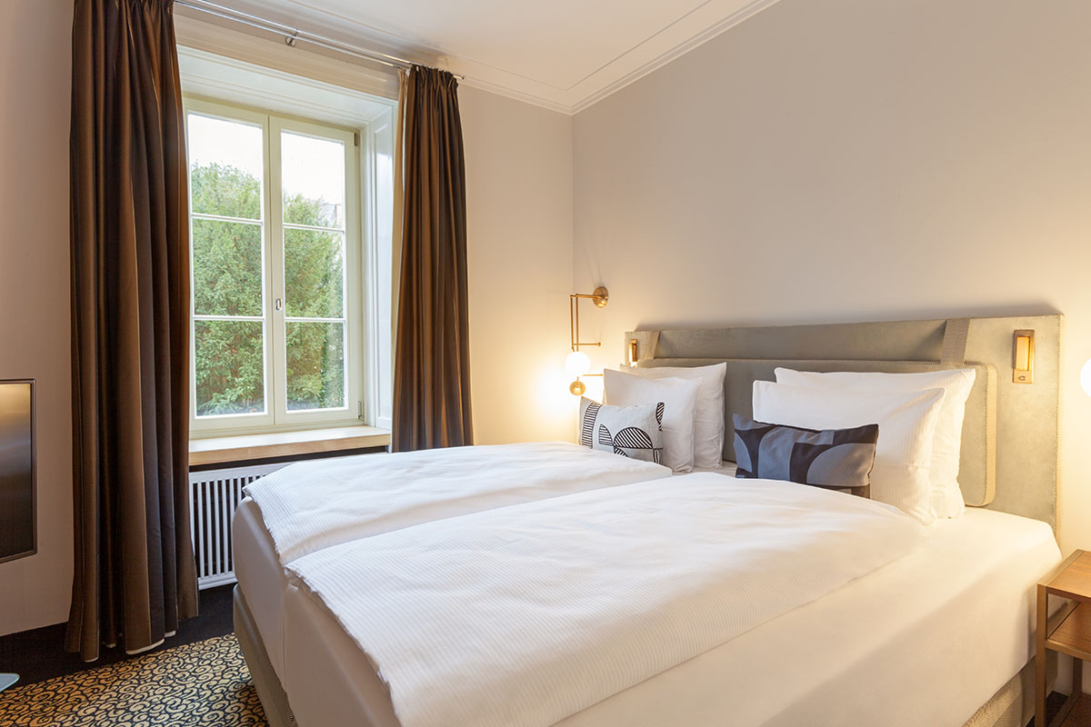 Comfortable double bed with luxurious bed linen and subtle color accents in the Thomas Mann Suite at Hotel Elephant.