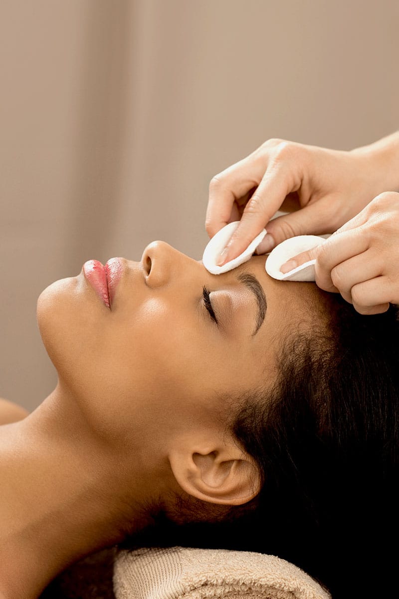 Kosmetikerin reinigt sanft das Gesicht einer Frau mit Wattepads für eine porentiefe Reinigung im Hotel Kaiserhof Heringsdorf.