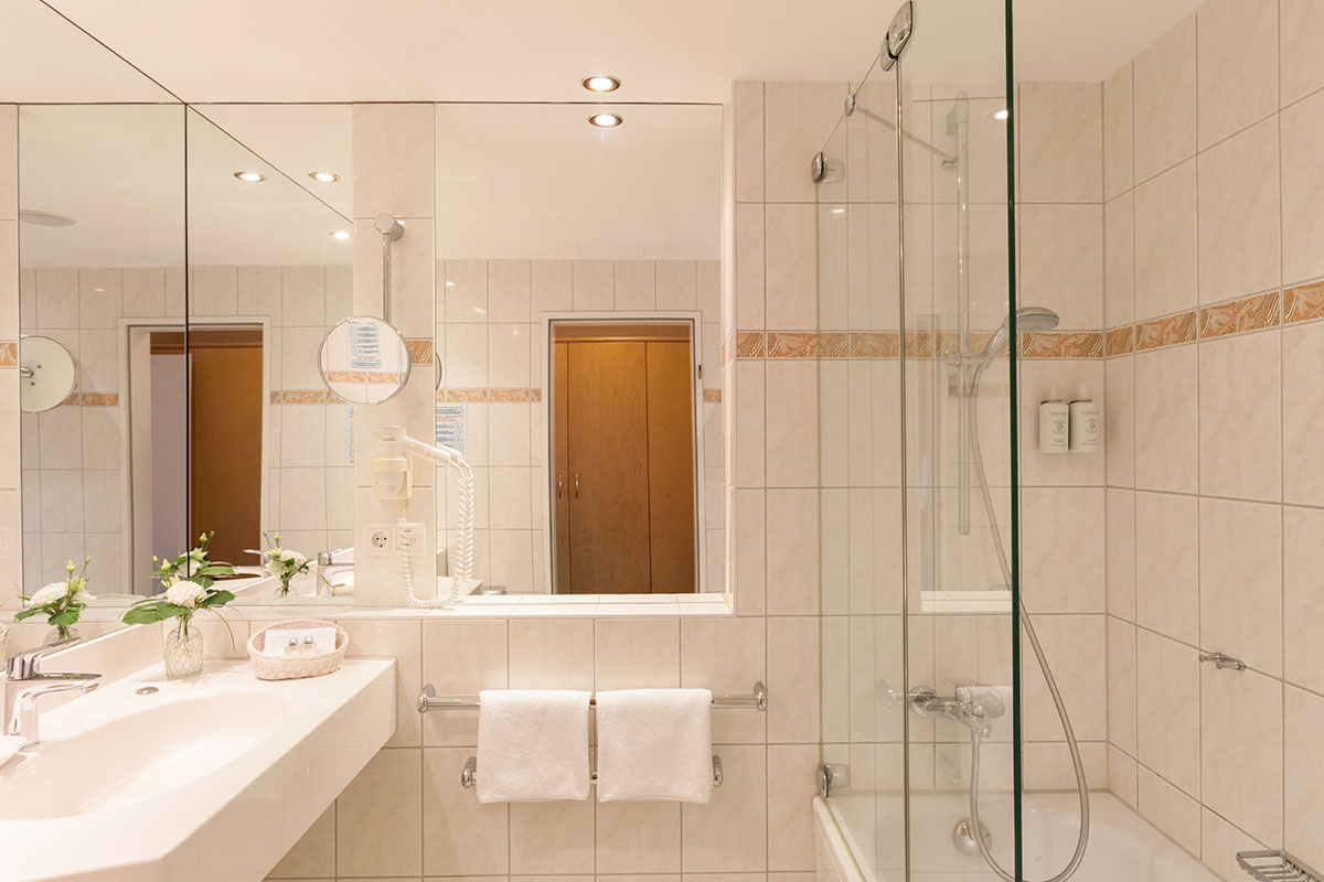 Spacious bathroom with bathtub, mirror wall and white tiles in the double room with balcony at the Hotel Kaiserhof.