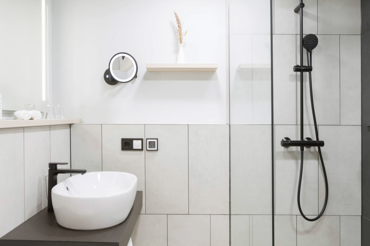 Modern bathroom with white washbasin, black tap and glass rain shower in a deluxe double room.