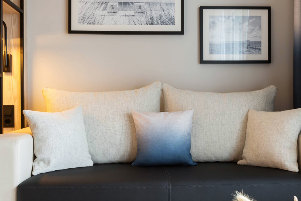 Bright sofa corner with decorative cushions and wall pictures in the background in the double room at the Hotel Kaiserhof Heringsdorf.