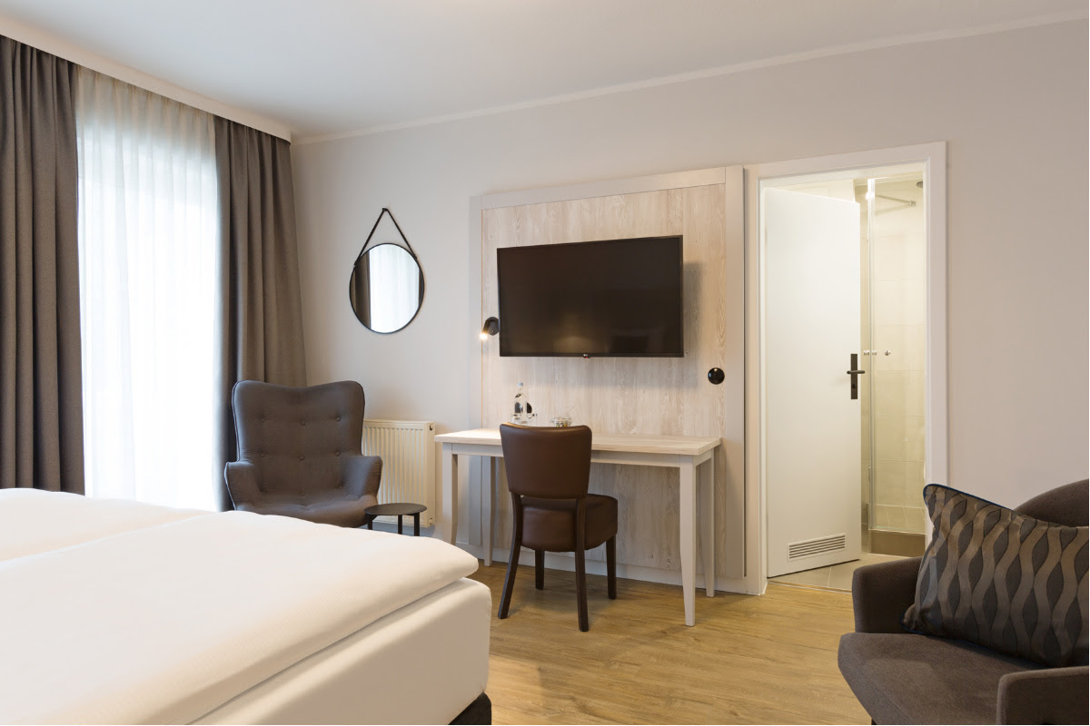 Modern furnished living area with TV, desk and seating in the double room at the Koopmanns Hotel.