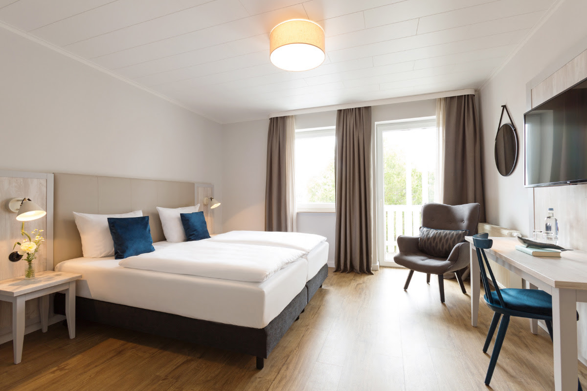 Bright double room at the Koopmanns Hotel with comfortable bed, balcony and work area, ideal for relaxing days on Rügen.
