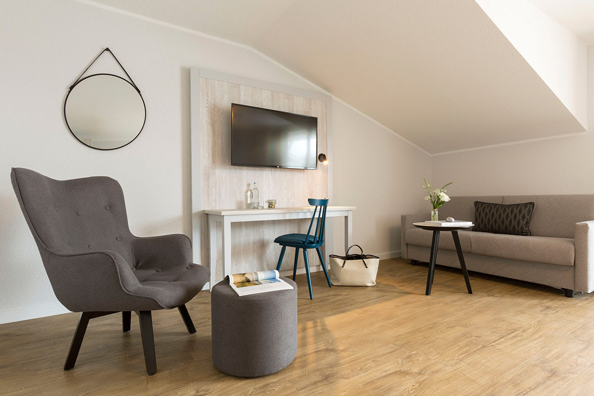 Comfortable living area of the superior double room at the Koopmanns Hotel with armchair, sofa, desk and TV.
