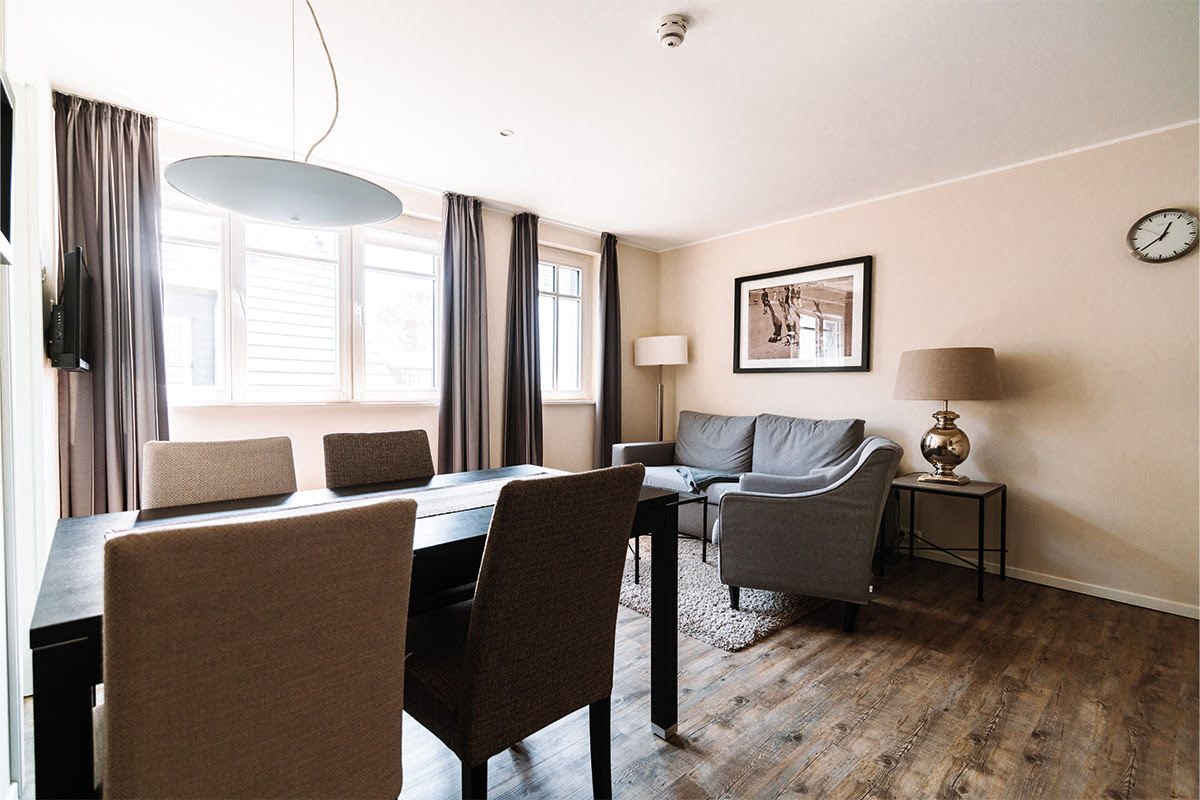 Living area with dining table, comfortable sofa and bright windows in the Strandblick vacation apartment in the Dünenpark in Ahrenshoop.